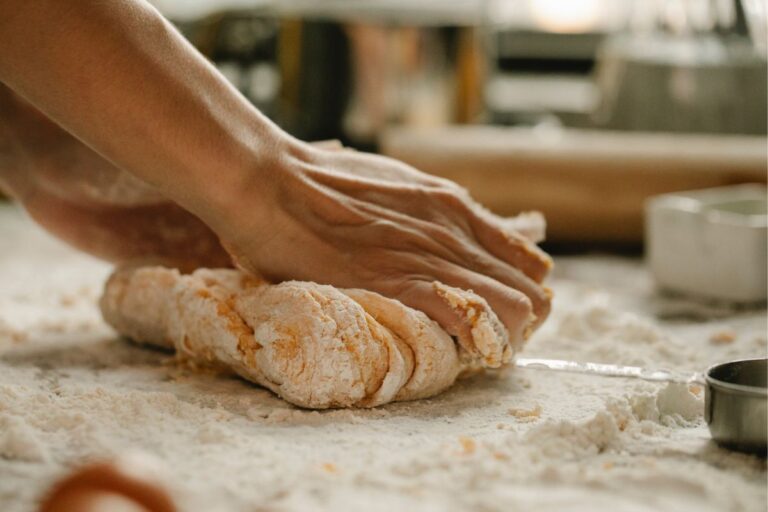 A woman's hands kneading a ball of dough on a wooden cutting board.