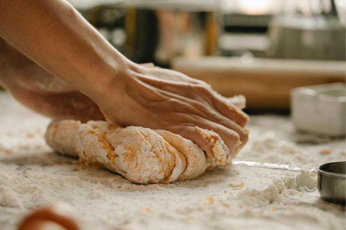 A woman's hands kneading a ball of dough on a wooden cutting board.